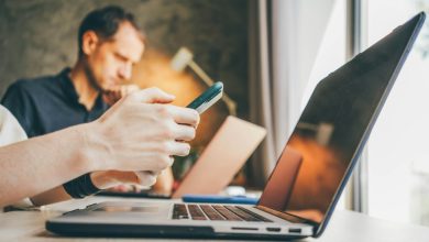 Businesswoman texts message on smartphone working on contemporary laptop