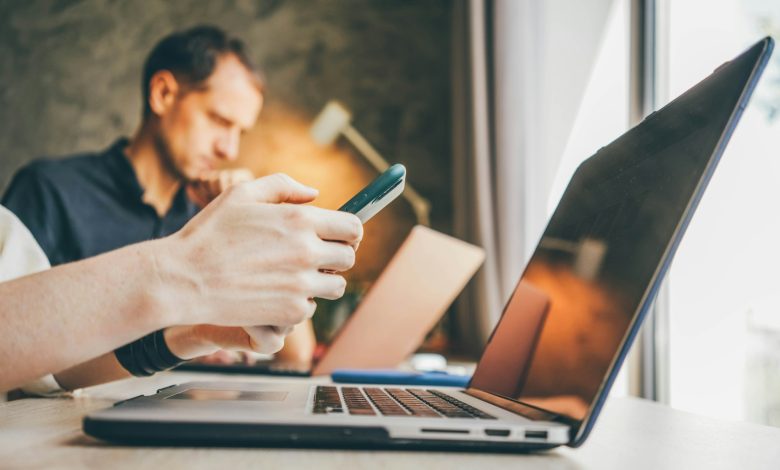 Businesswoman texts message on smartphone working on contemporary laptop