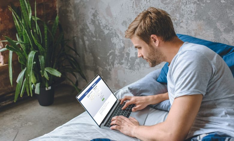 young man in bed using laptop with facebook on screen