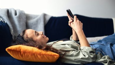 Young Smiling Woman Relaxing At Home Lying On Sofa Checking Social Media On Mobile Phone